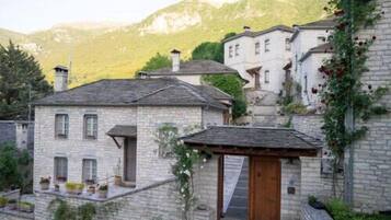 A stone building with a wooden door, surrounded by greenery and a mountain in the background.