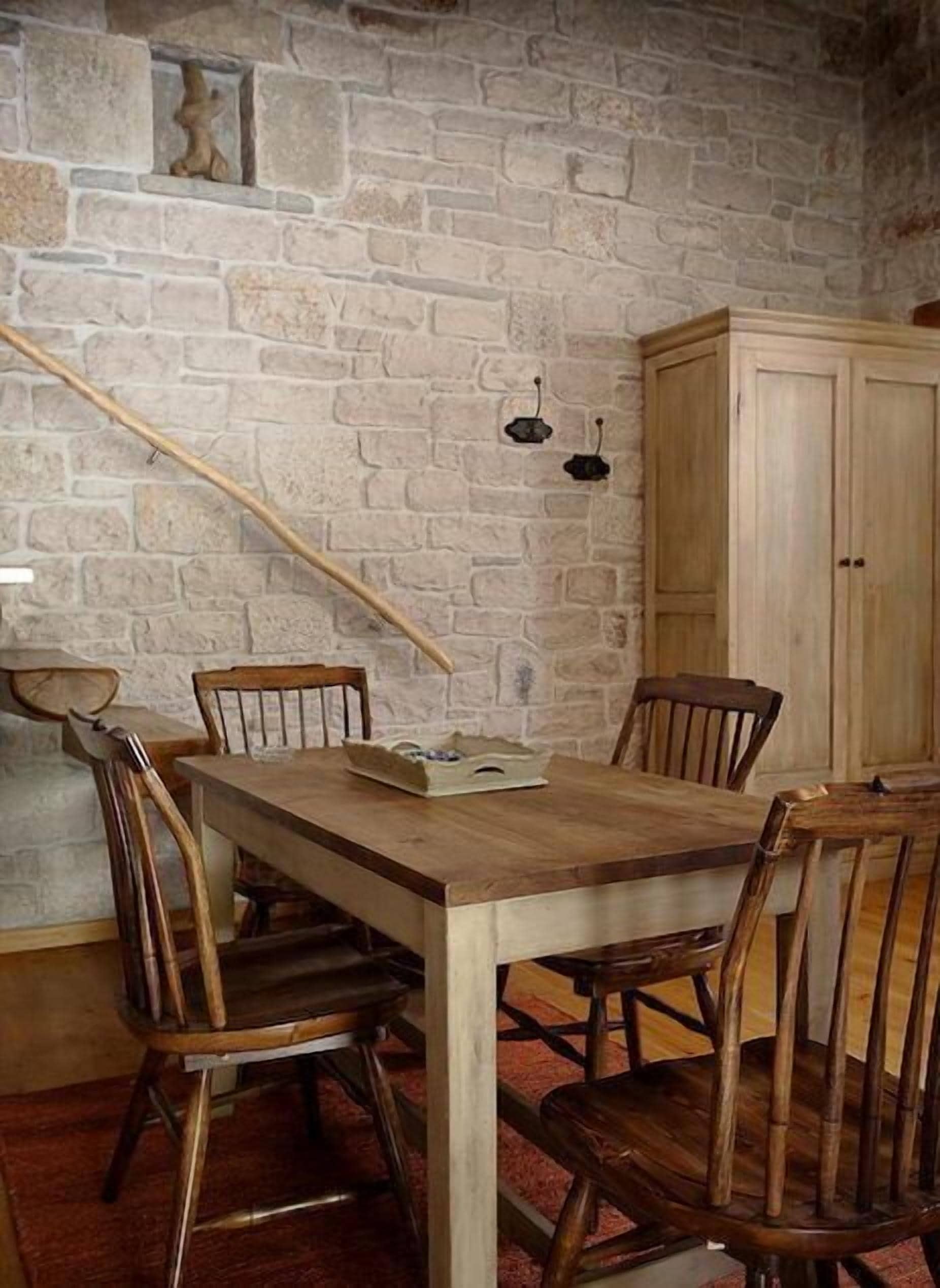 Un comedor rústico con pared de piedra, mesa de madera y sillas.