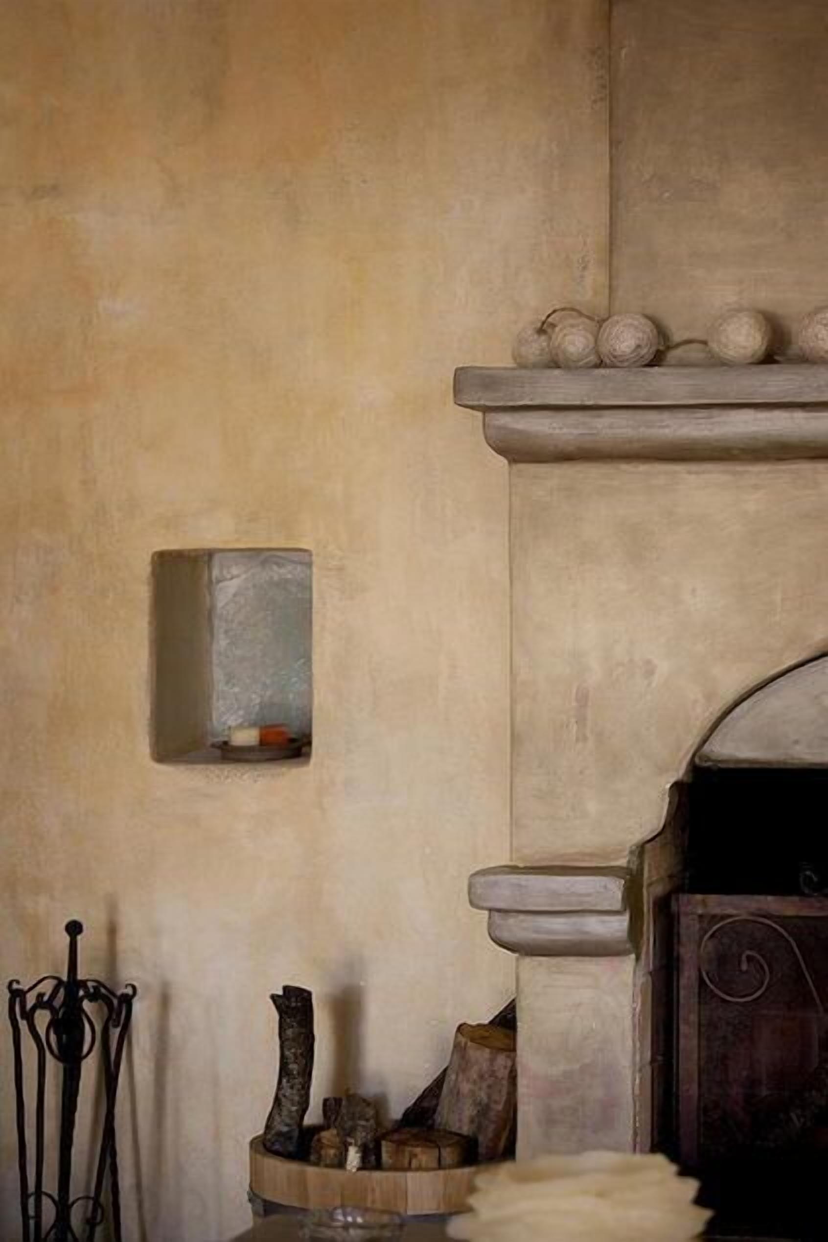 A rustic interior with a stone fireplace, a small shelf with decorative items, and a metal stand with a candle.