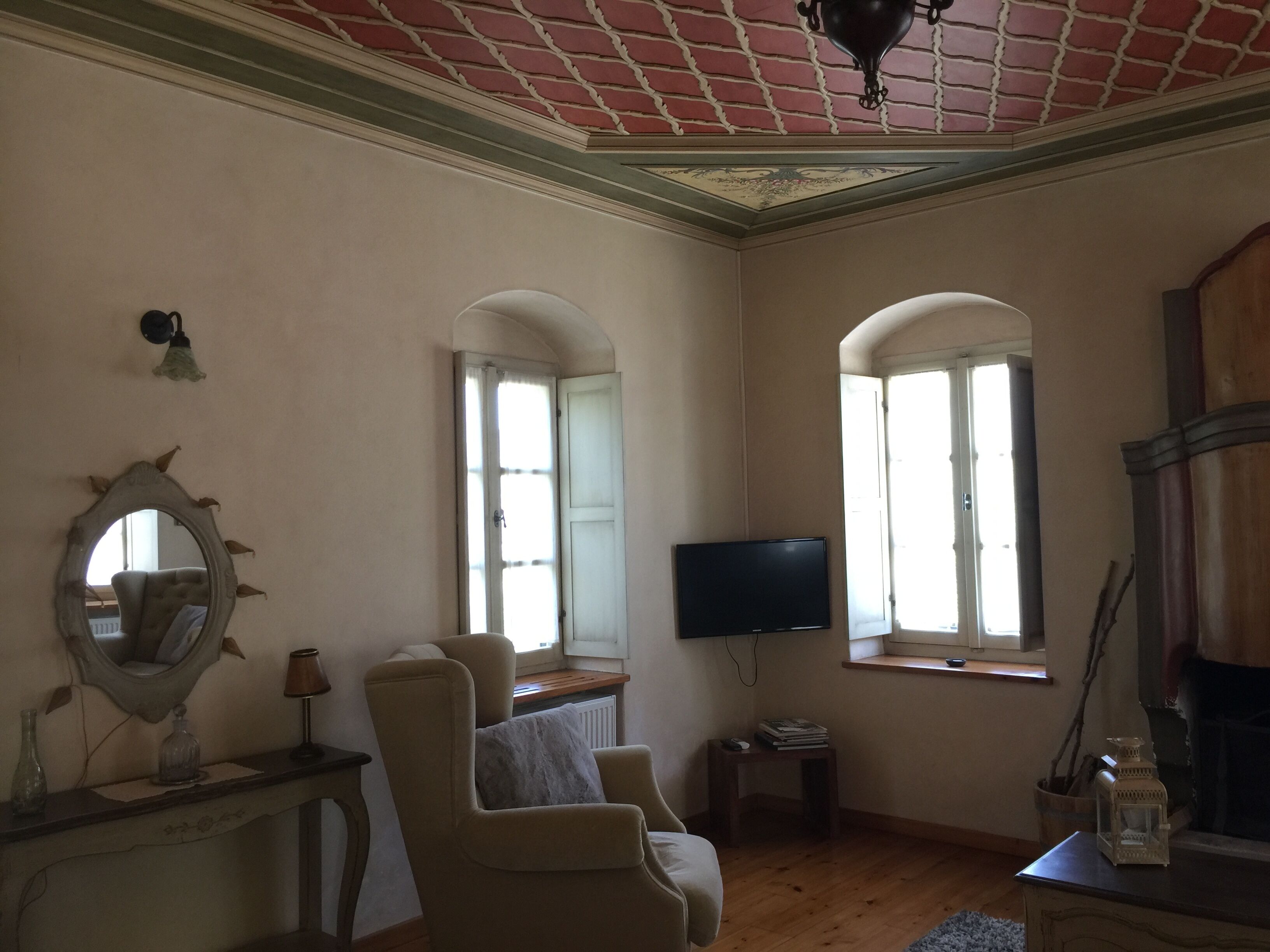 Un salon avec une télévision, deux fauteuils, une cheminée et un miroir au mur.