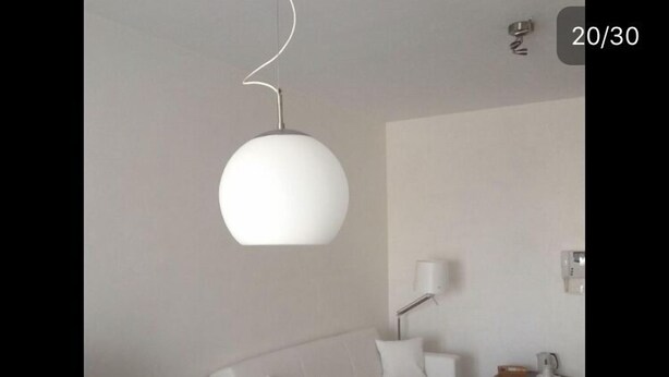 A modern living room with a white sofa, a dining table with a plant, and a hanging light fixture.
