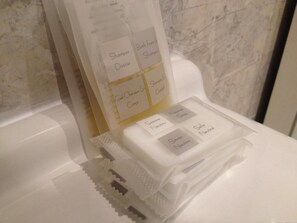 A bathroom with a white sink and a mirror. There are toiletries on the counter, including a bottle of shampoo and a bar of soap.