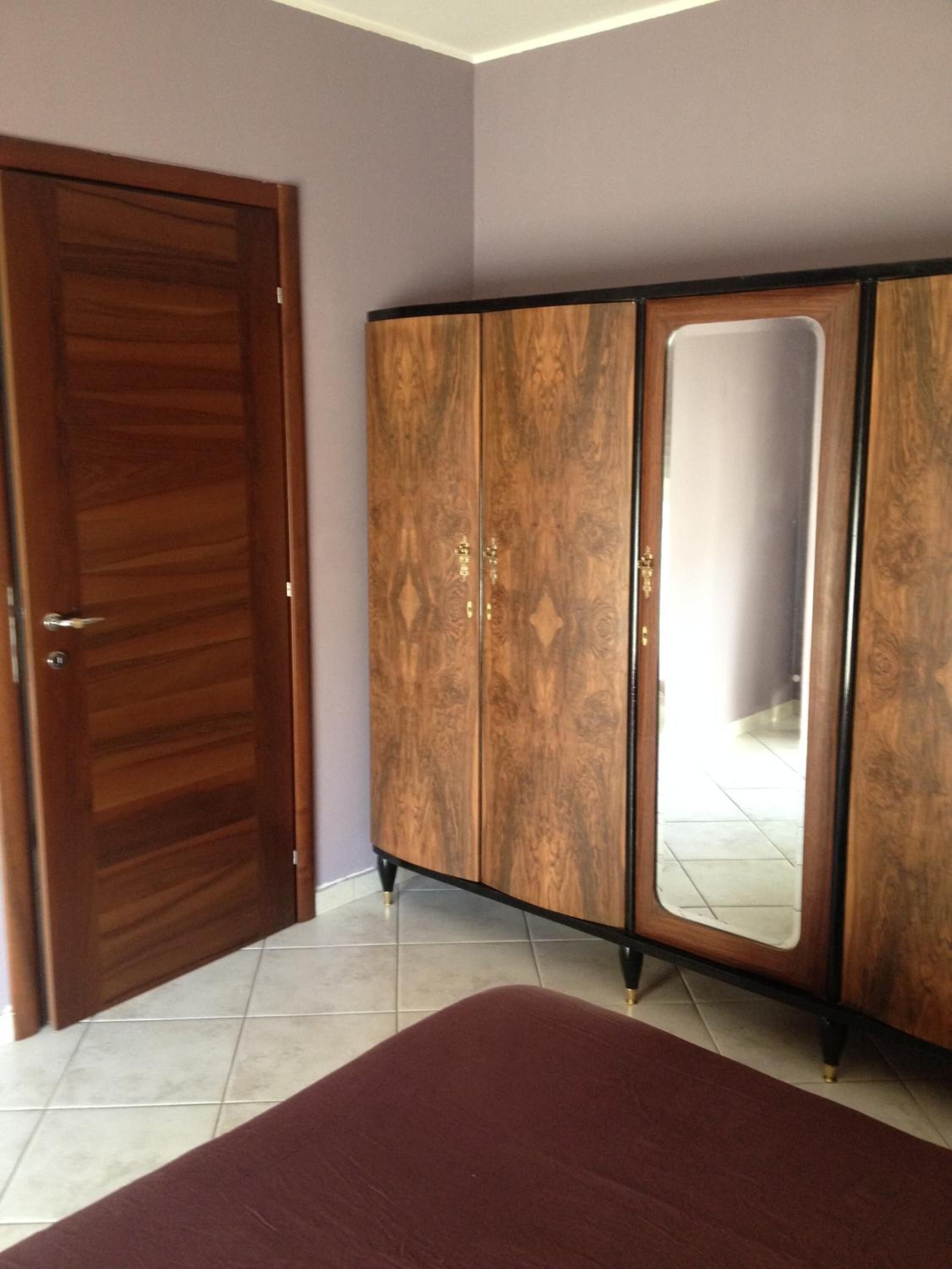 A bedroom with a wooden wardrobe, a large mirror, and a bed with a red bedspread.