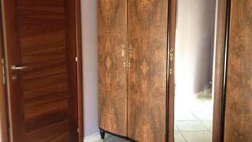 A bedroom with a wooden wardrobe, a large mirror, and a bed with a red bedspread.
