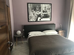 A bedroom with a large bed, a bedside table, a wall-mounted picture, and a door. - B&B via Roma suite (Ortona)