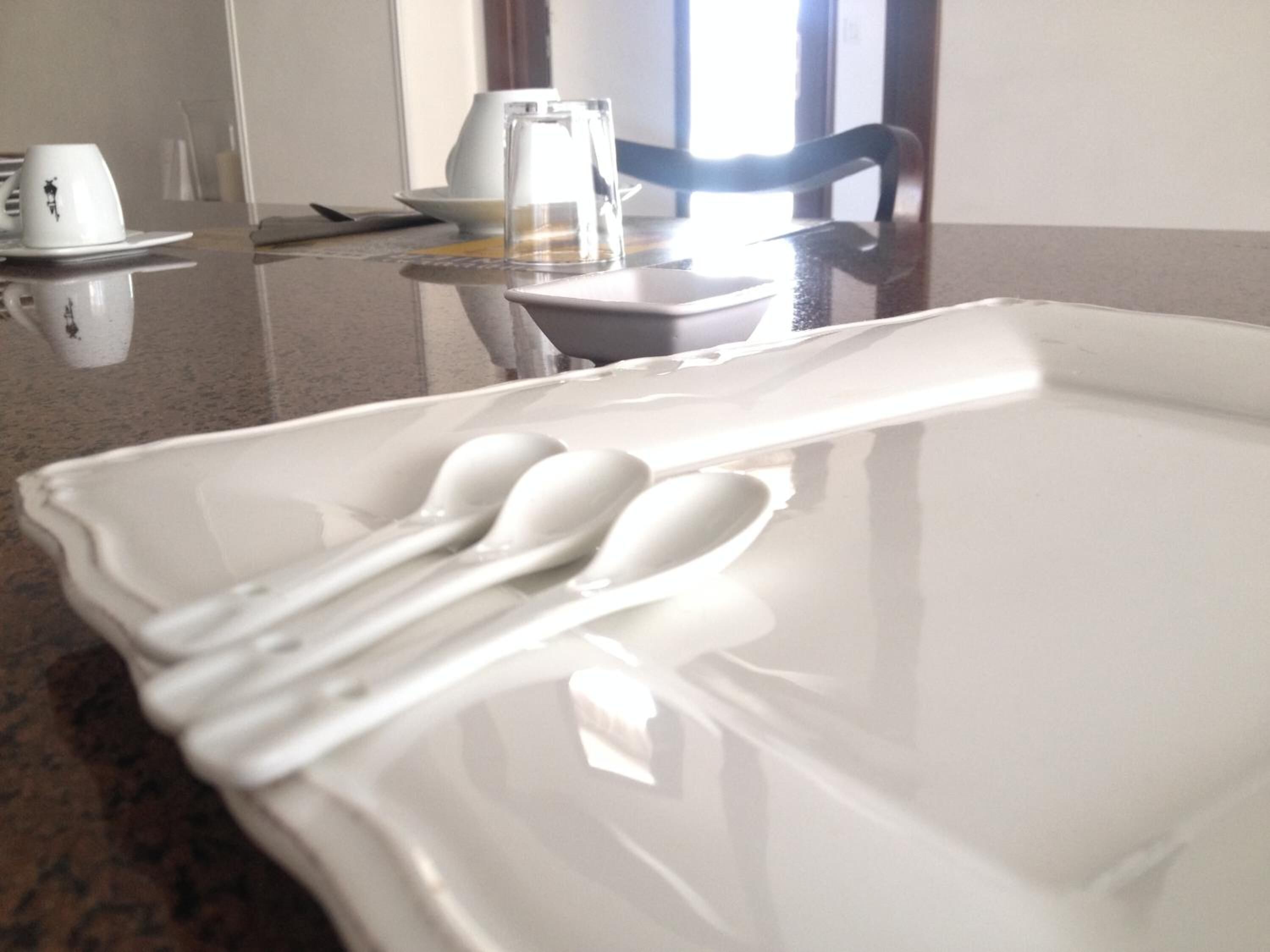 Una mesa de comedor con un plato blanco, tres cucharas blancas y un vaso.