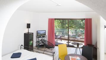 A hotel room with a bed, a desk with a computer, a chair, a small table, and a view of the outdoors.