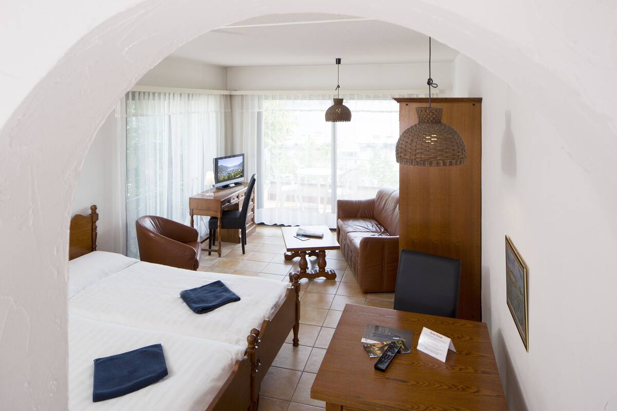 A hotel room with a bed, a desk, a chair, a sofa, and a table.
