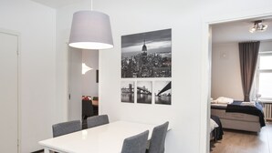En moderne stue med en hvid sofa, et spisebord med grå stole og et stort vindue med gardiner.
