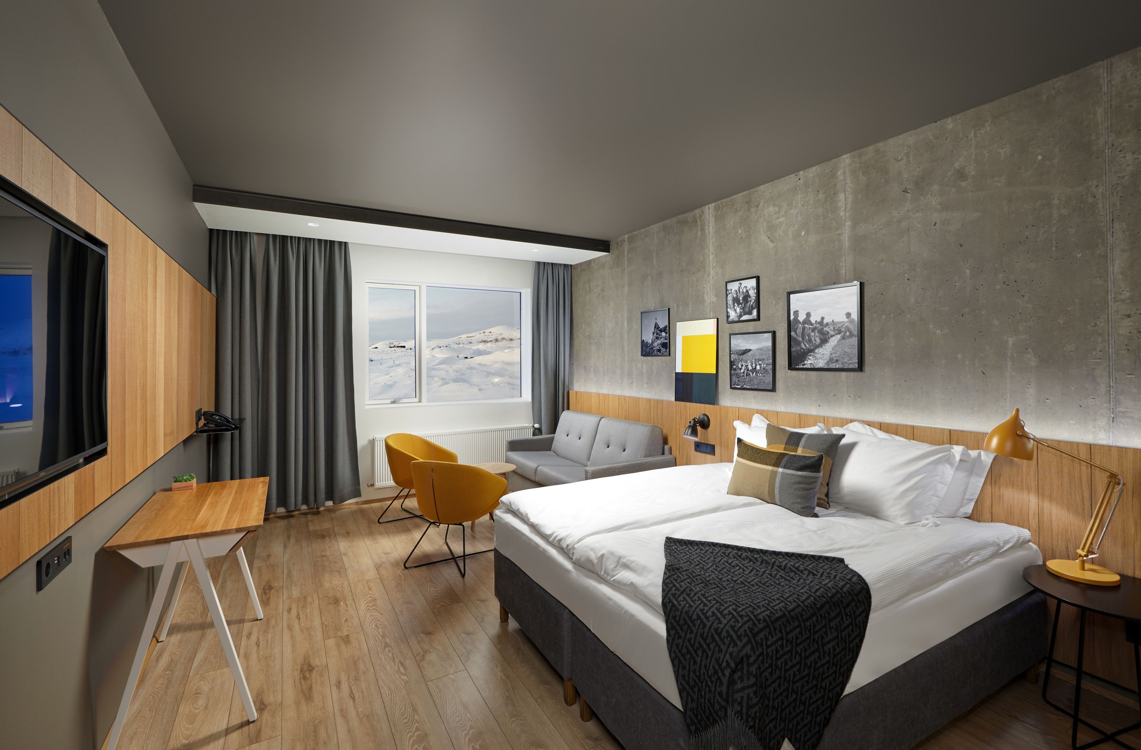 A modern hotel room with a large bed, a desk, a chair, and a TV.