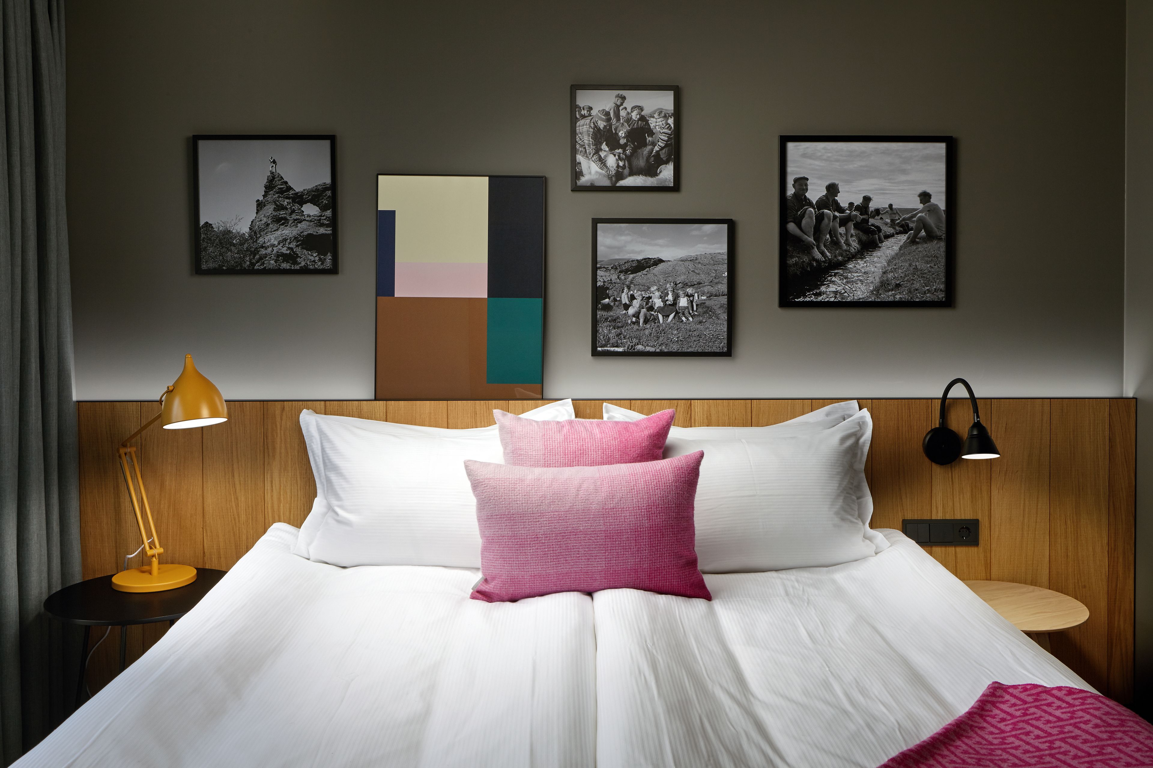 Een hotelkamer met een groot bed, een nachtkastje met een lamp, en een wand met ingelijste foto's.