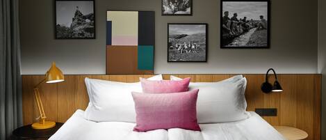 A hotel room with a large bed, a nightstand with a lamp, and a wall with framed pictures.