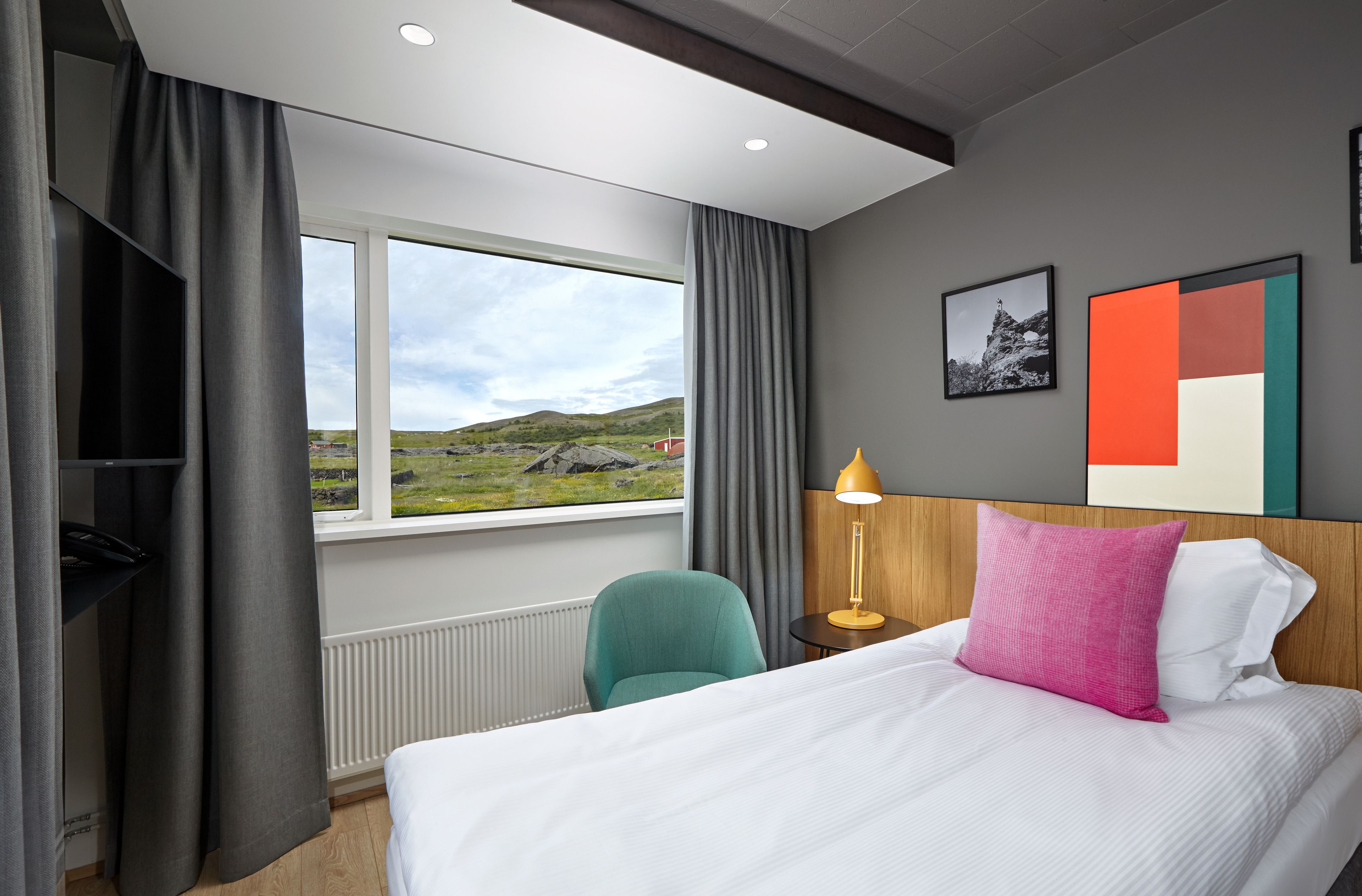 Ein Hotelzimmer mit Bett, Sessel, Nachttisch, Lampe, Fernseher und einem Fenster mit Landschaftsblick.
