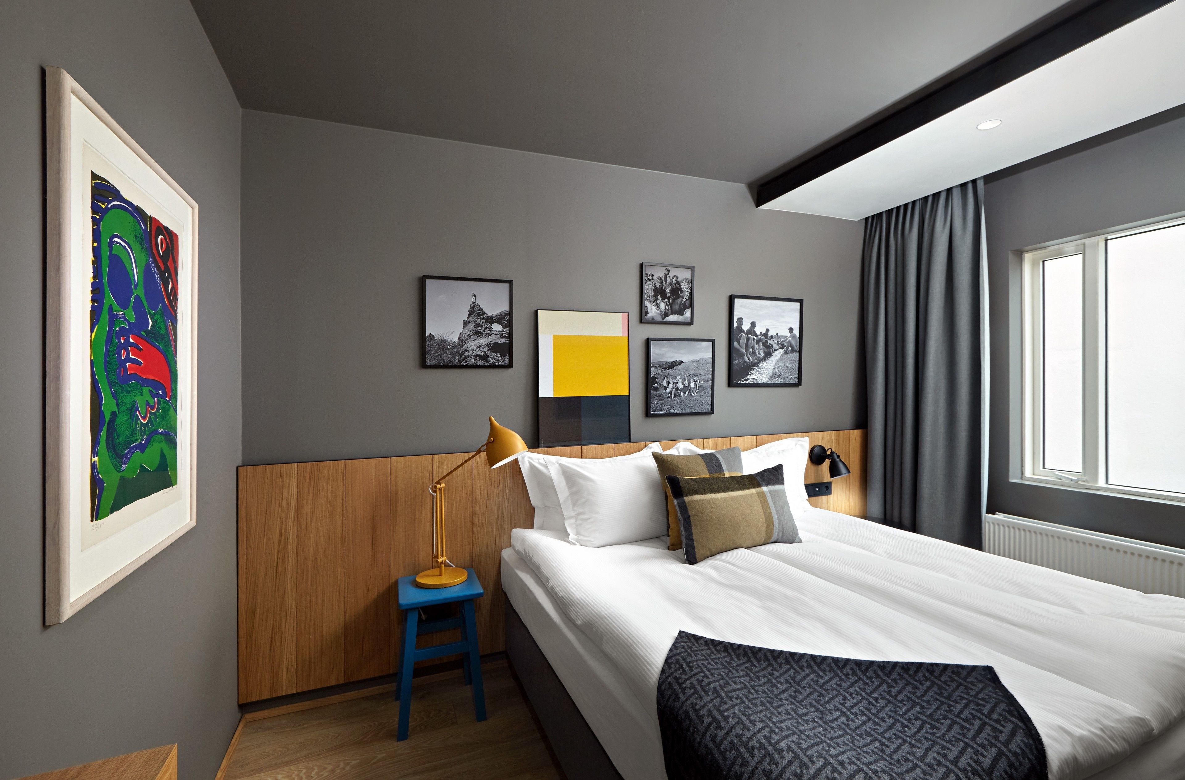 A modern hotel room with a neatly made bed, a side table with a lamp, and a large window with curtains.