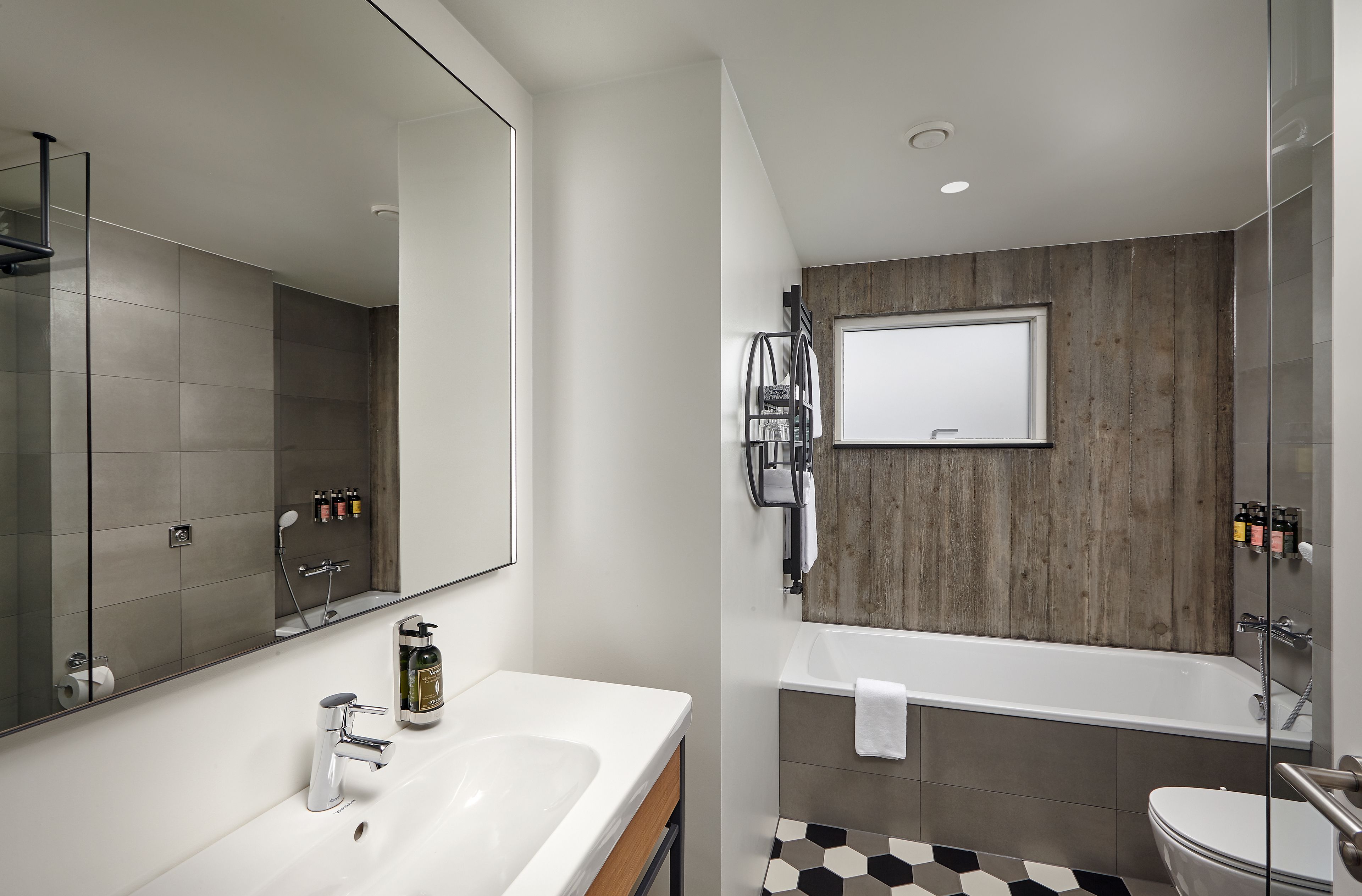 A modern bathroom with a large mirror, a white sink, a bathtub, and a toilet.