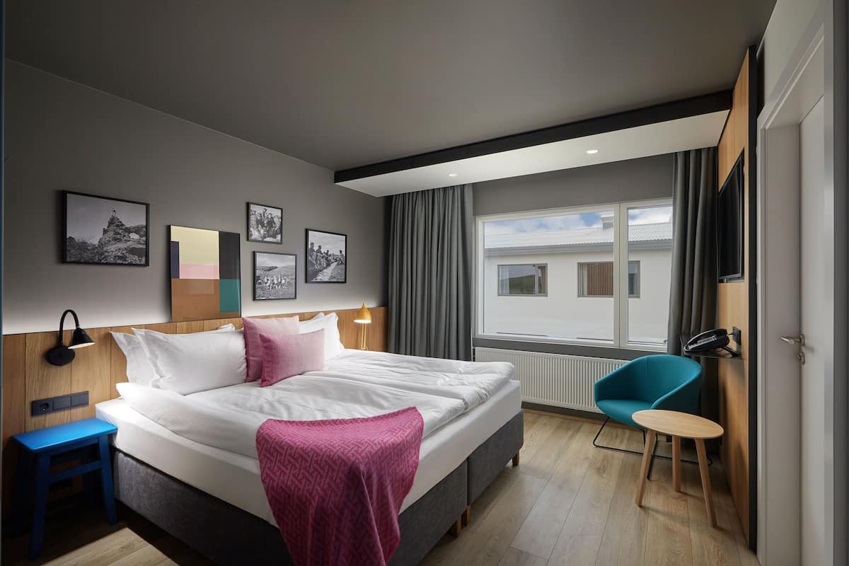 Ein modernes Hotelzimmer mit einem großen Bett, einem Schreibtisch, einem Stuhl und einem Fenster mit Vorhängen.