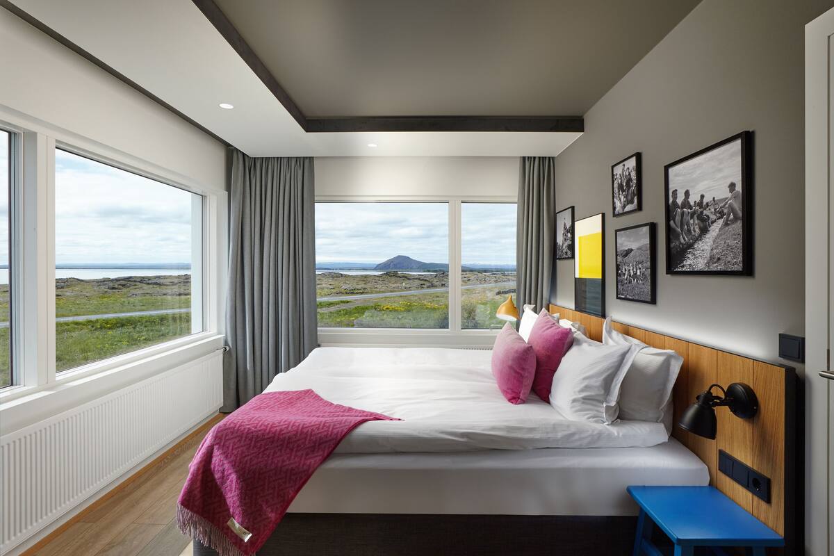 Ein modernes Hotelzimmer mit einem großen Bett, Blick auf die Landschaft und Kunstwerken an der Wand.