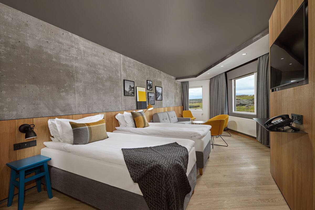 Ein modernes Hotelzimmer mit zwei Betten, einem Schreibtisch, einem Sessel, einem Fernseher und einem großen Fenster mit Blick.