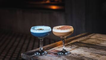 Dos cócteles sobre una mesa de madera con una chimenea al fondo.