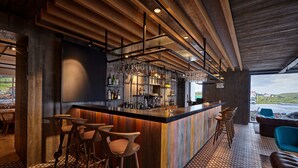 Un espace bar moderne avec un comptoir en bois, des tabourets et une vue sur l’extérieur.