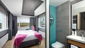 Una habitación de hotel moderna con una cama grande, vistas a una iglesia distante y un baño con lavabo y espejo.