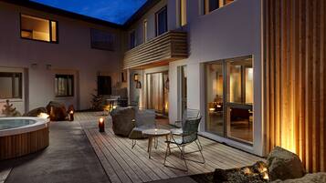A modern outdoor patio with a hot tub, seating area, and large windows.