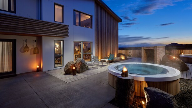 Une maison moderne dotée d’un jacuzzi, d’un espace salon extérieur et d’une grande fenêtre donnant sur le paysage.