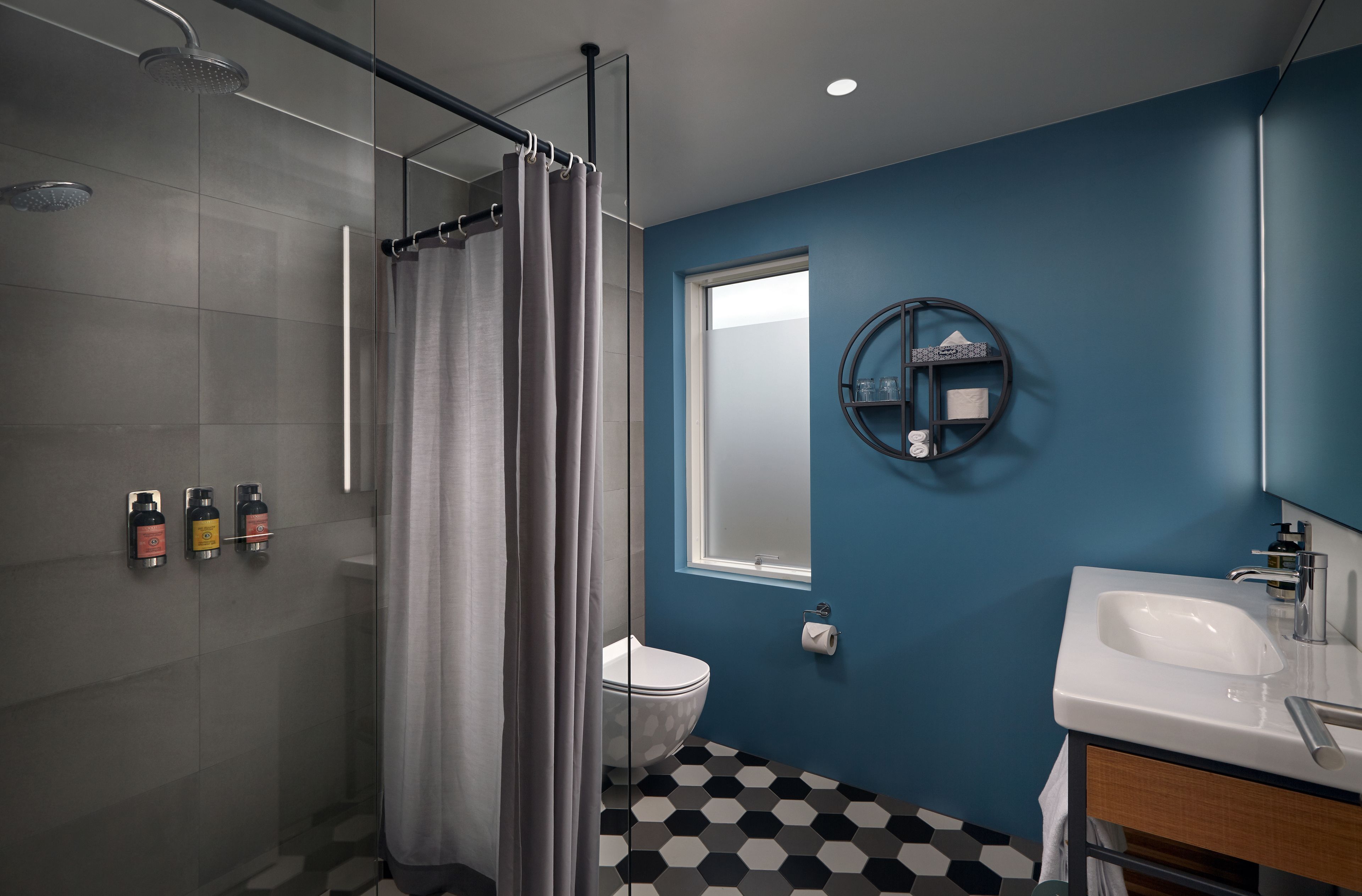 A modern bathroom with a glass shower enclosure, a toilet, a sink with a mirror, and a blue accent wall.