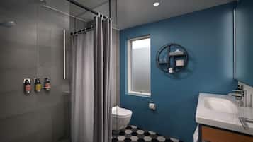 A modern bathroom with a glass shower enclosure, a toilet, a sink with a mirror, and a blue accent wall.
