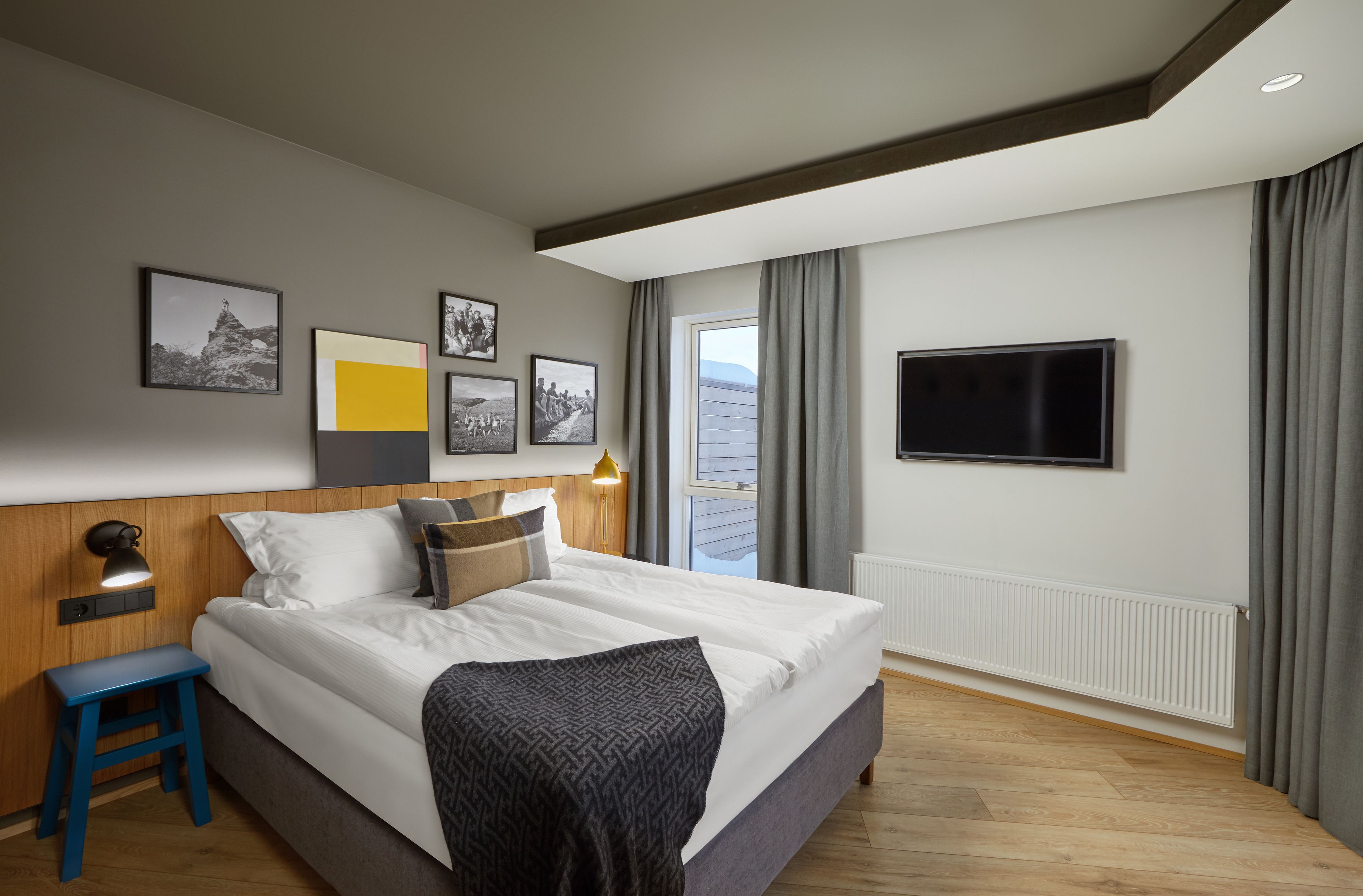 A modern hotel room with a large bed, a TV, and a window with curtains.