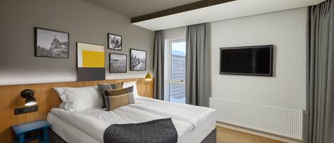A modern hotel room with a large bed, a TV, and a window with curtains.