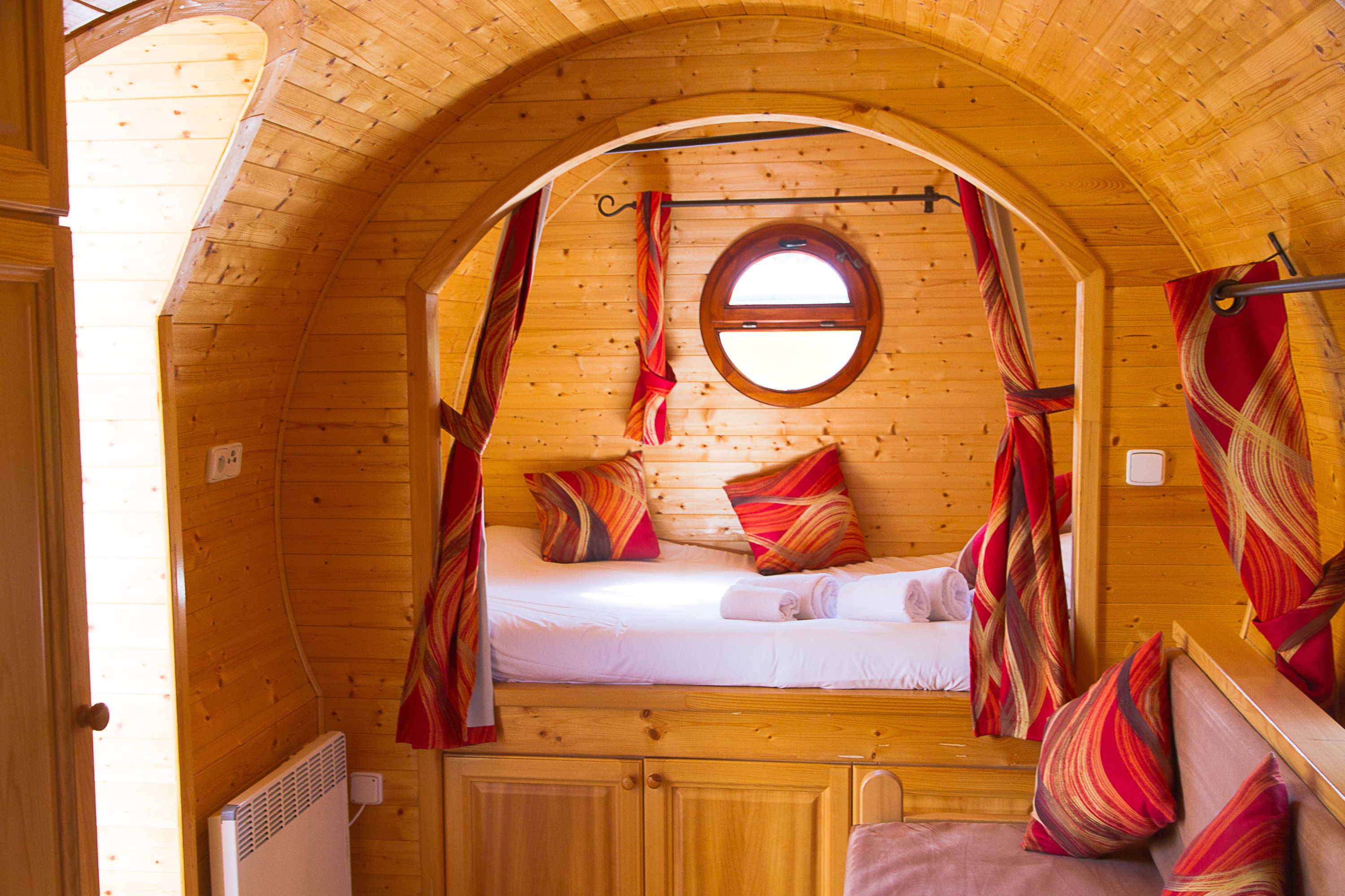 A cozy, circular wooden room with a bed, pillows, and curtains.