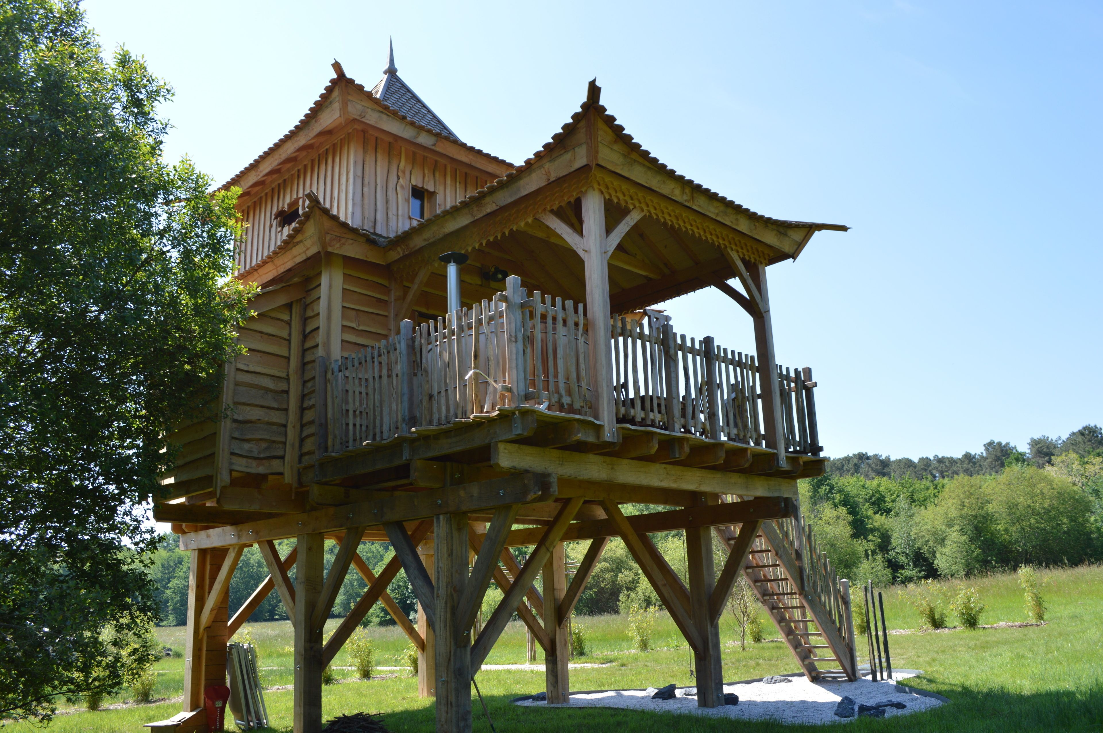 A wooden structure with a balcony and a roof, surrounded by greenery.