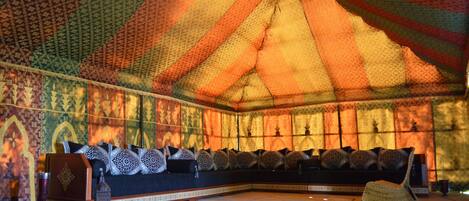 A room with a large, colorful tent-like structure, a sofa with patterned cushions, and a woven chair.