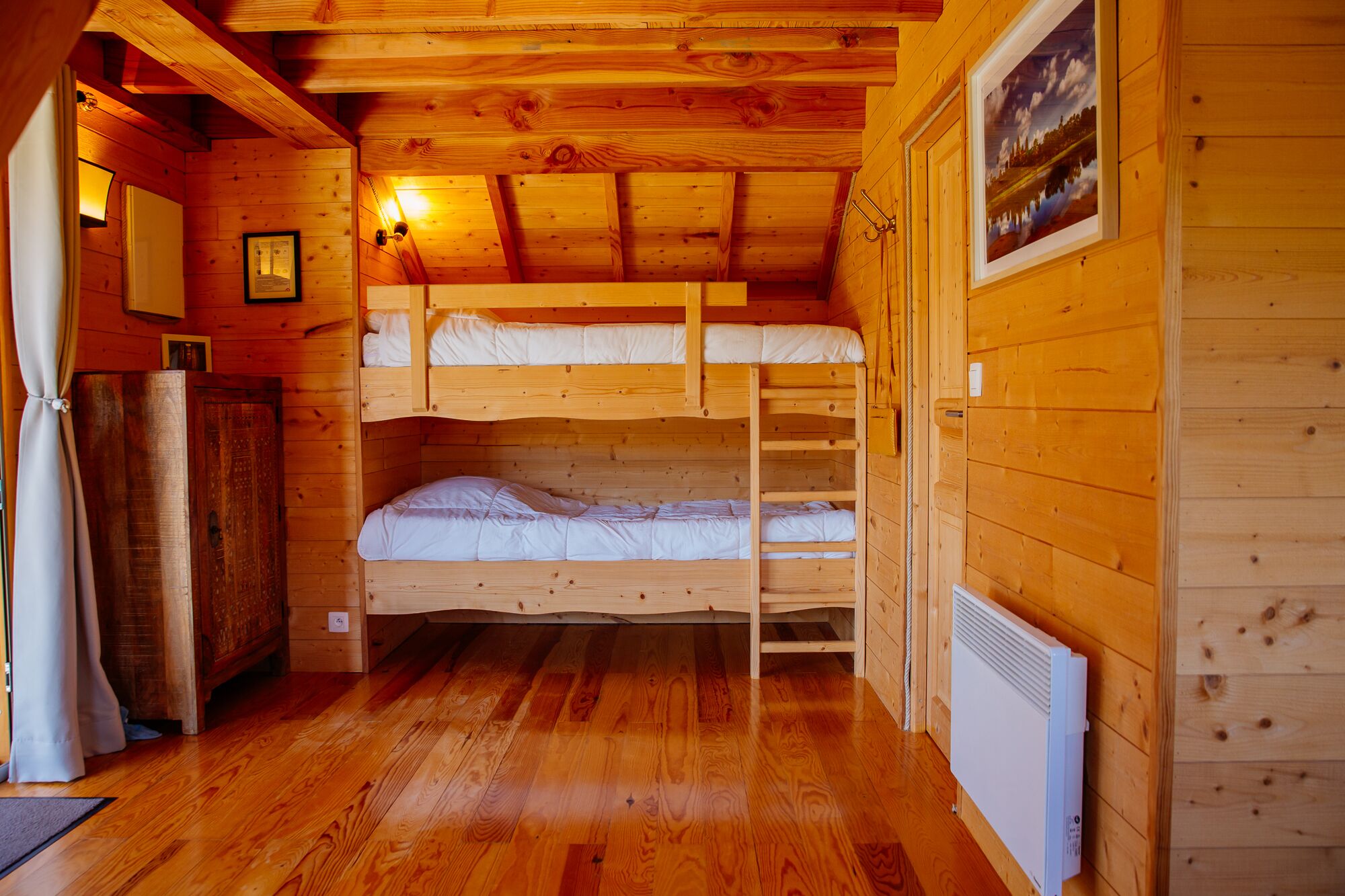 A cabin with a bunk bed, wooden walls, a radiator, and a framed picture on the wall.