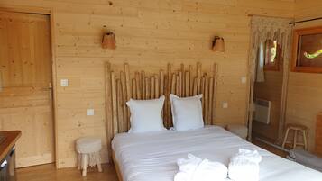 Un dormitorio de cabaña de madera con una cama, dos almohadas, un taburete pequeño y un calentador.