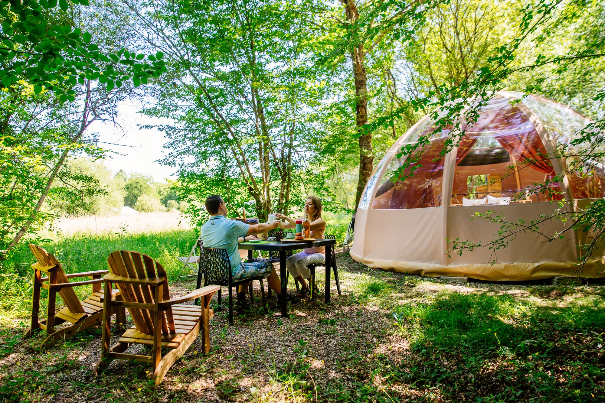 A tented area with a table and chairs, surrounded by trees.
