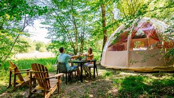 A tented area with a table and chairs, surrounded by trees.