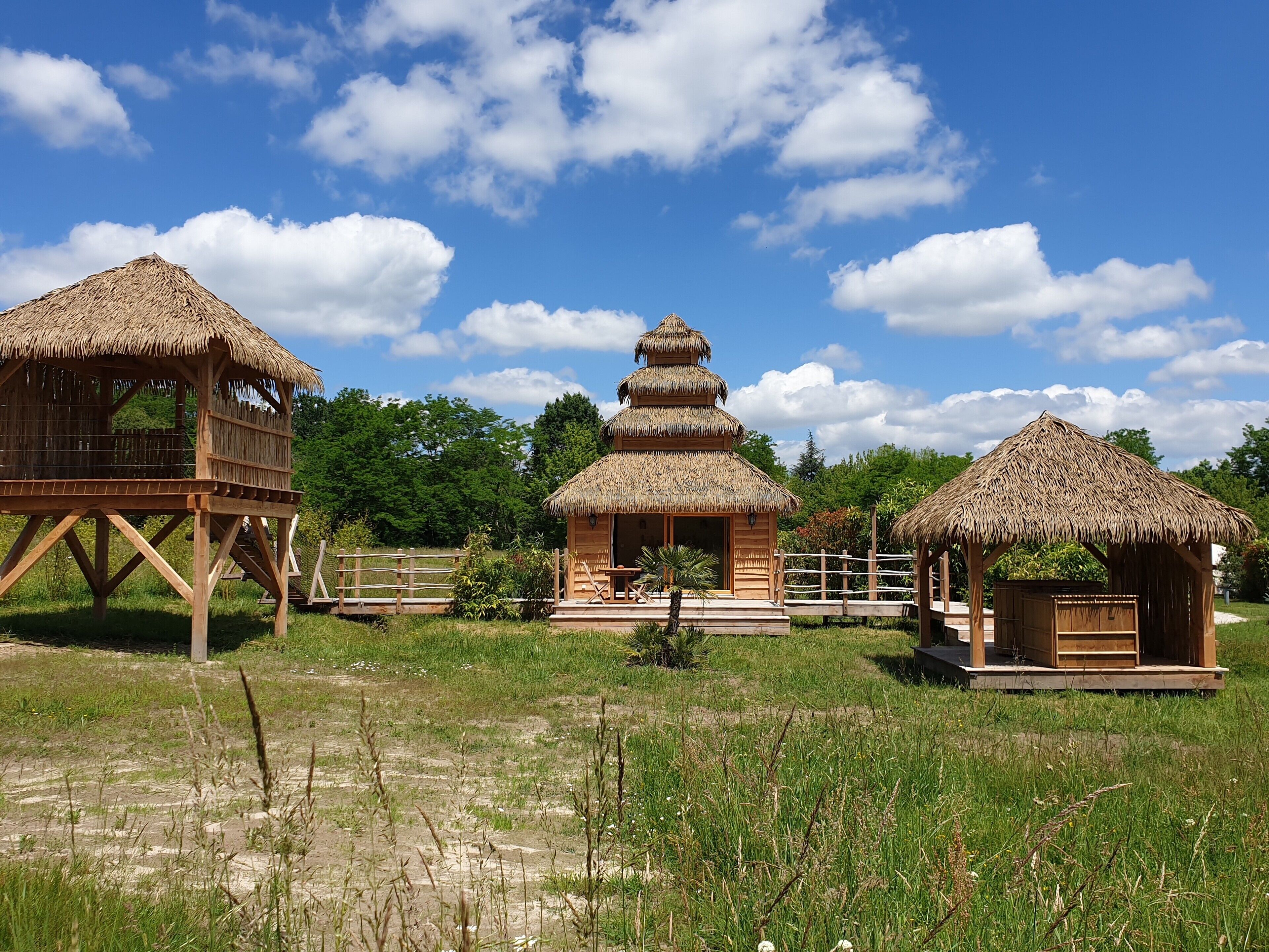 A thatched-roof structure with a tiered design, a wooden deck, and a fenced area with a bench.