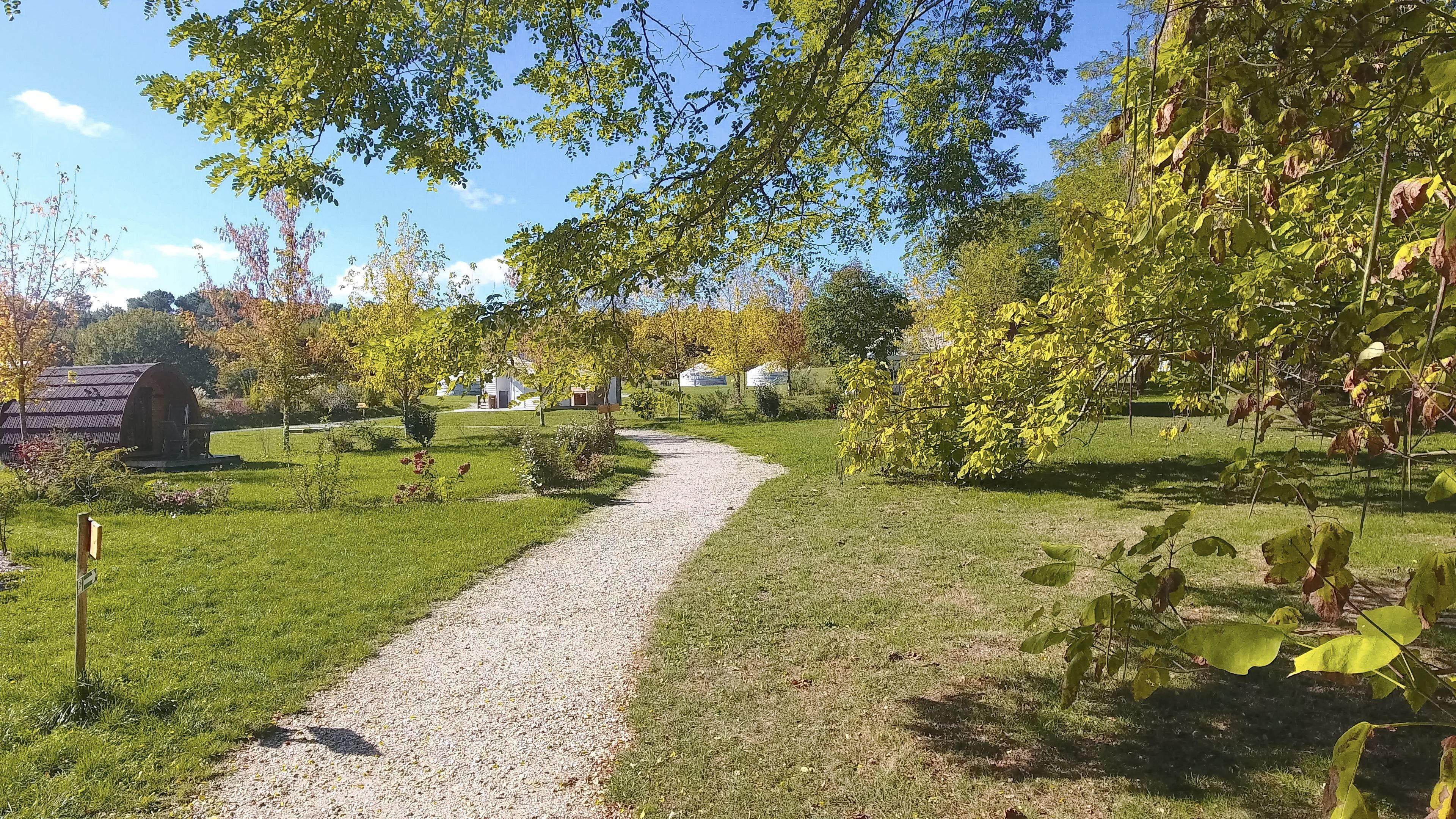 A gravel path leading through a grassy area with trees and a small building structure in the background.