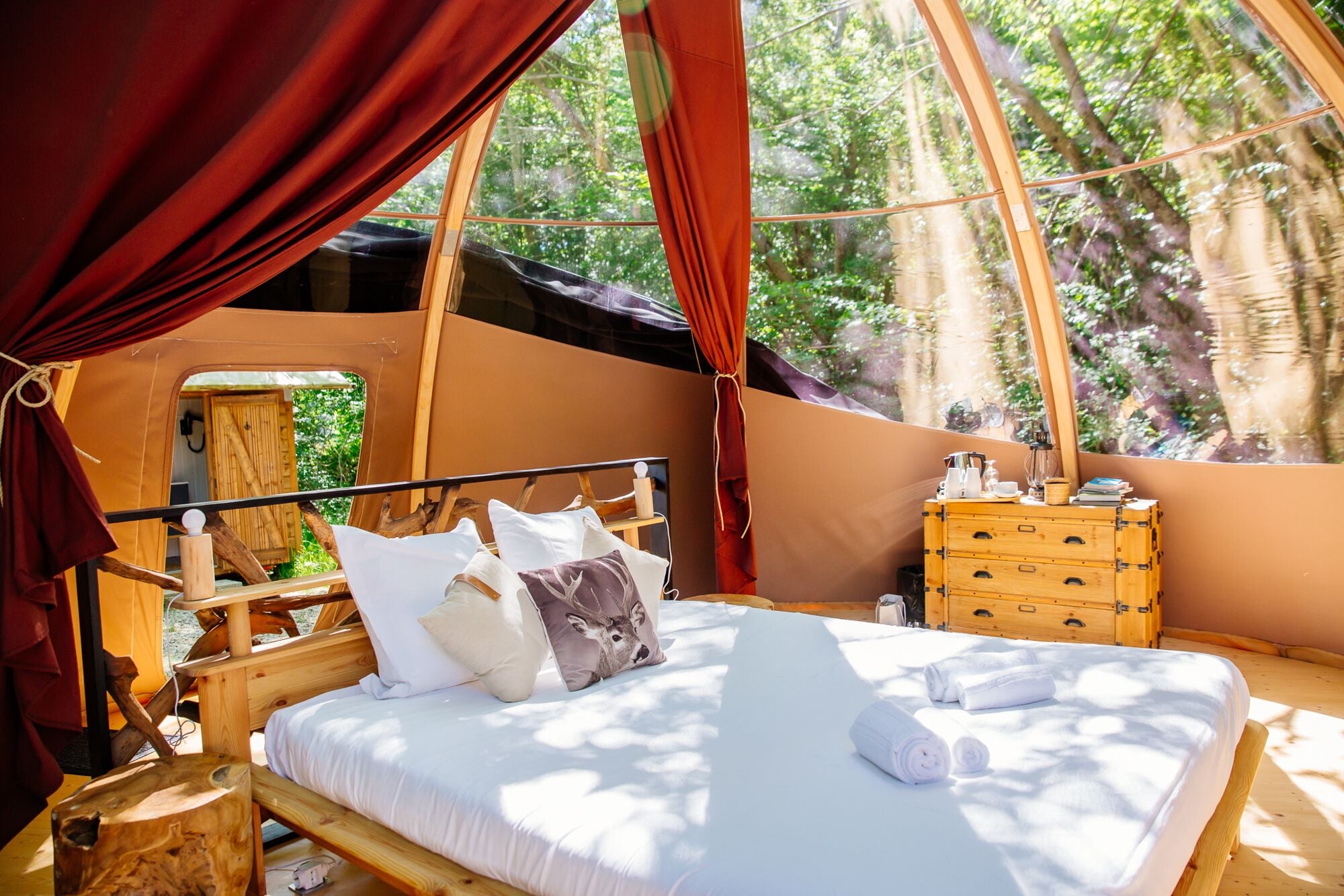 A cozy tent with a bed, wooden dresser, and a small table.