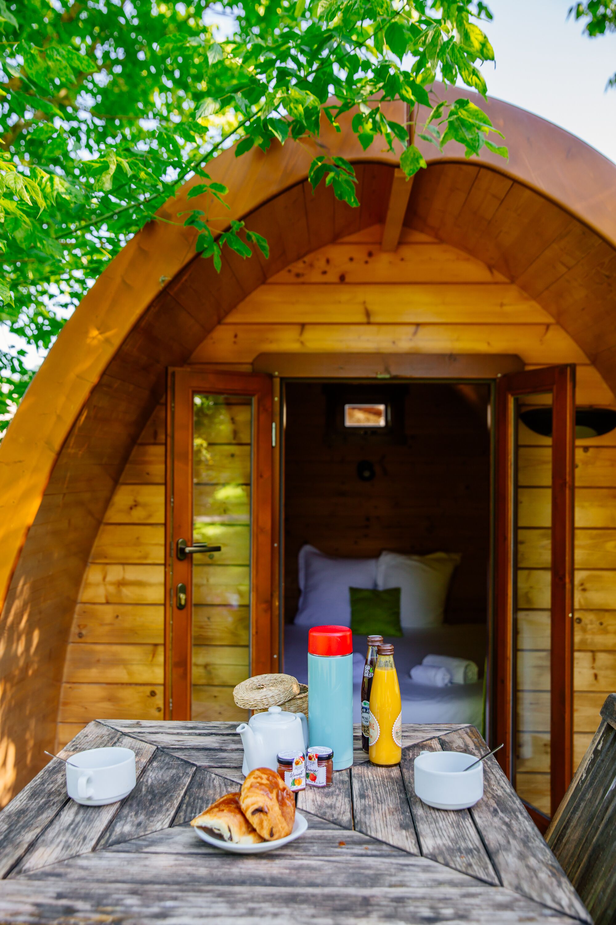 A cozy wooden cabin with a dining table set for breakfast, including pastries, a kettle, and a bottle of juice.