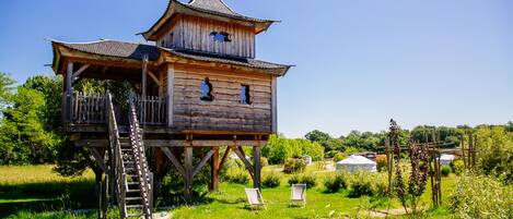 A wooden tower with a balcony and a ladder, surrounded by a grassy area with two chairs.