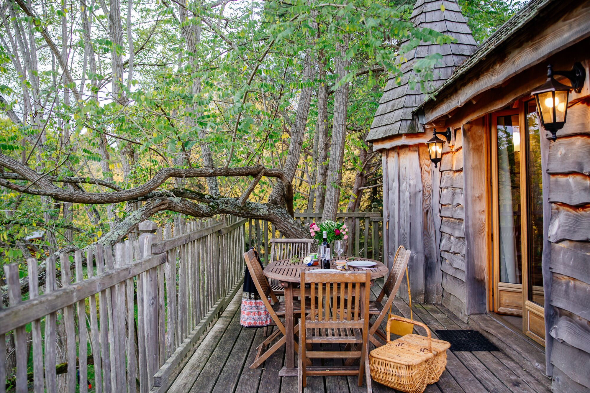 Une terrasse en bois avec une table et des chaises, entourée d’une clôture en bois et d’arbres.