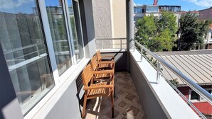 A balcony with a wooden table and chairs, large windows, and a view of neighboring buildings and trees. - Armoni City Hotel (Istanbul)