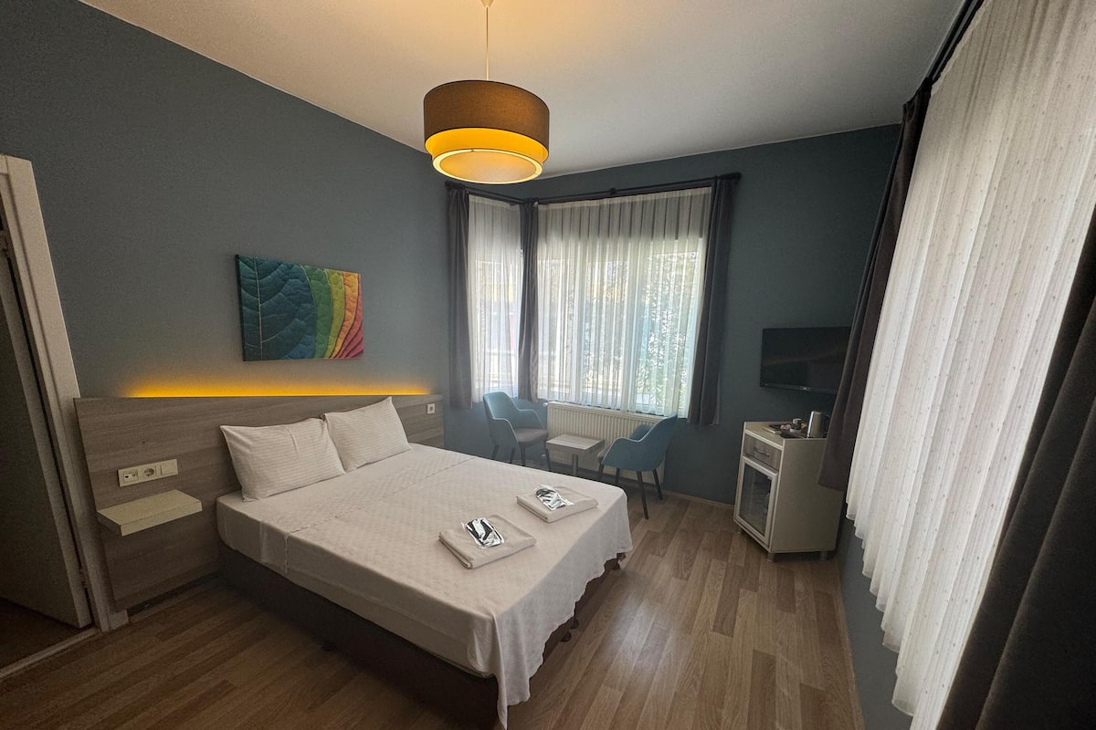 A hotel room with a bed, bedside table, desk, chair, and a TV.