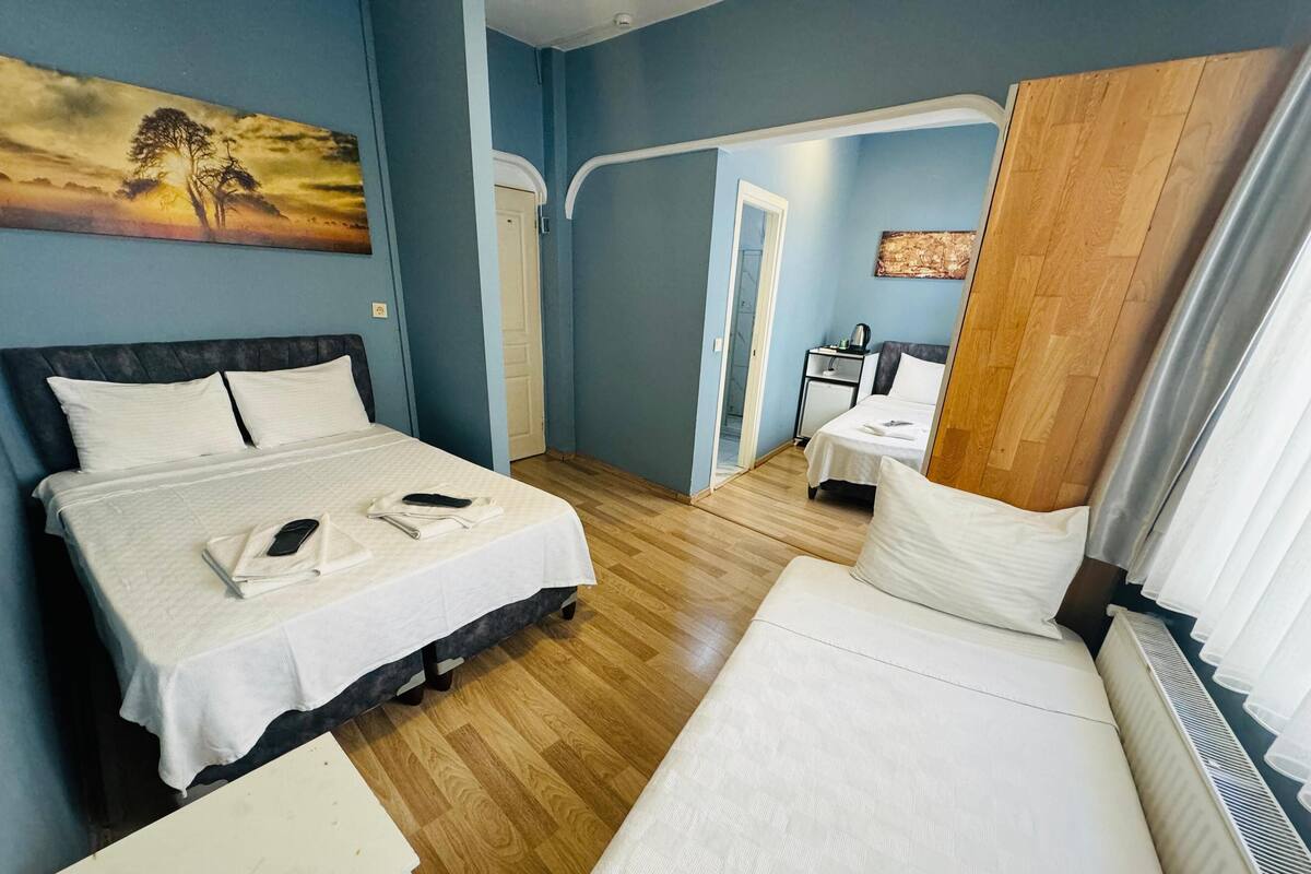 A hotel room with two beds, a wooden floor, a painting on the wall, and a small table with a chair.