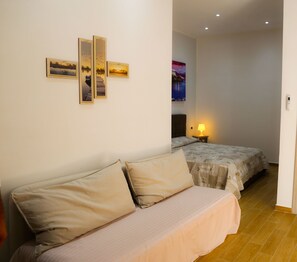 A bedroom with two beds, a nightstand with a lamp, and three framed pictures on the wall. - Caracciolo109 (Naples)