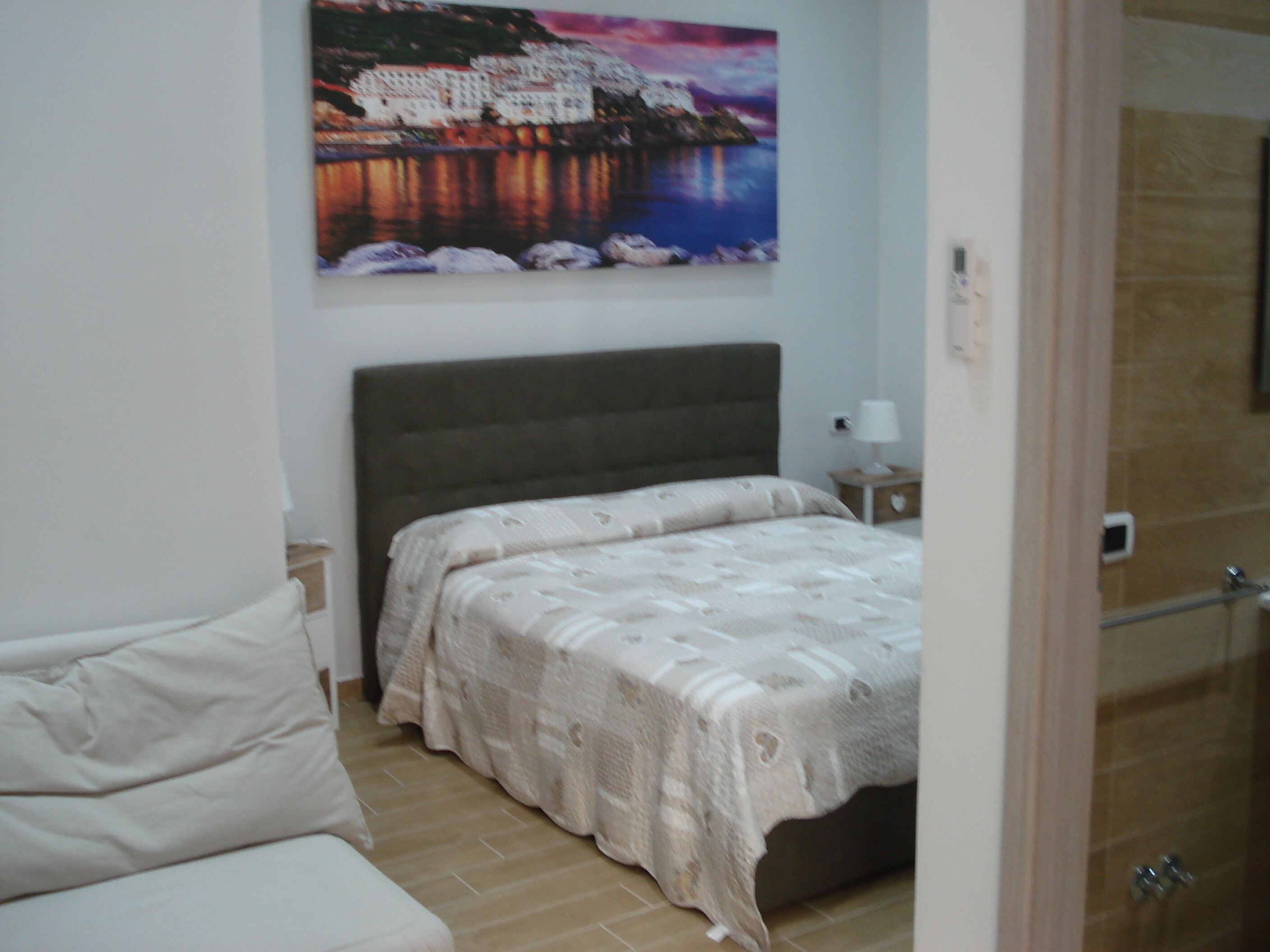 A bedroom with a bed, a nightstand, a painting on the wall, and a door.