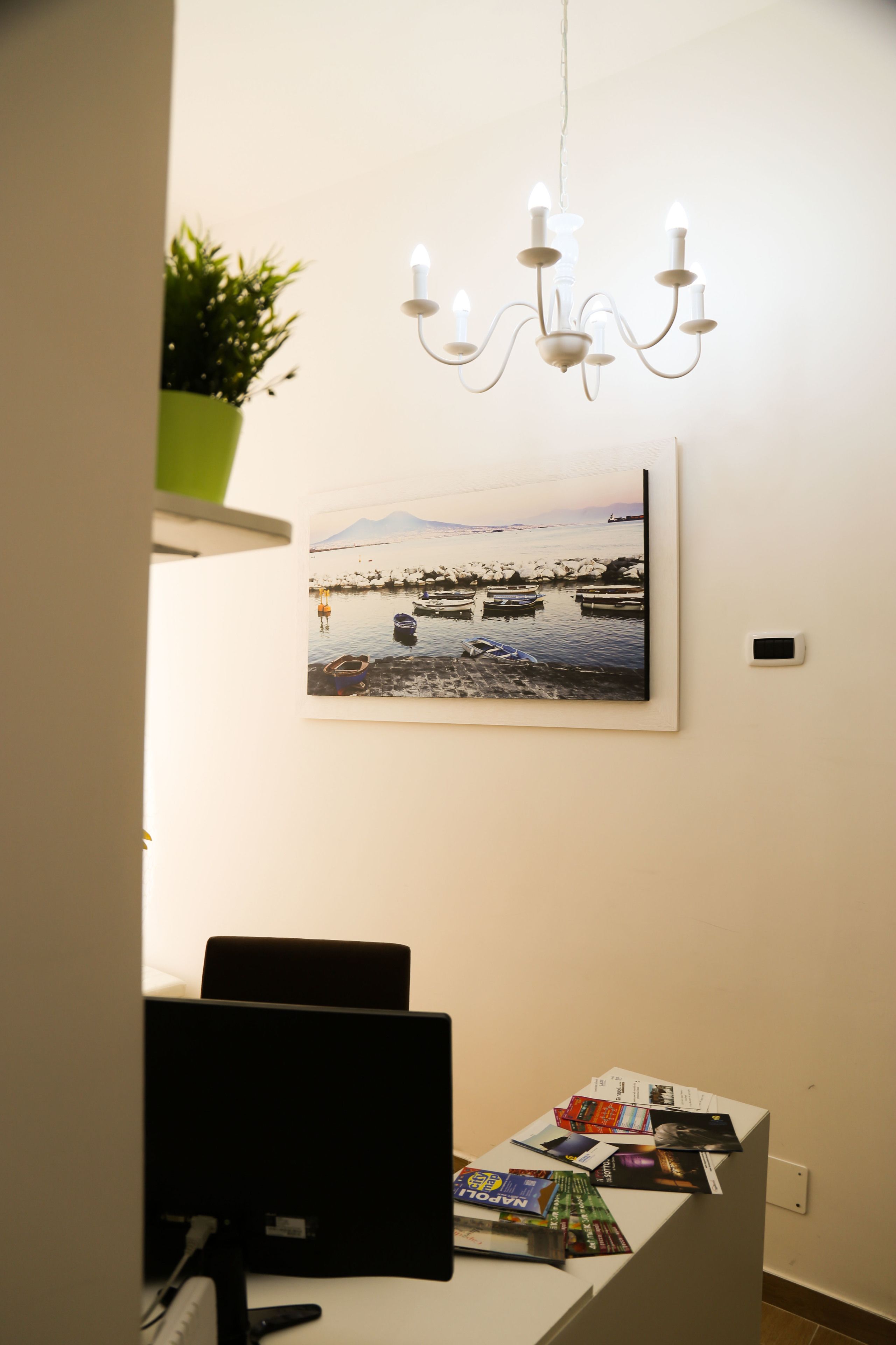 A reception desk with a computer, a framed photograph of boats on water, and a hanging light fixture.
